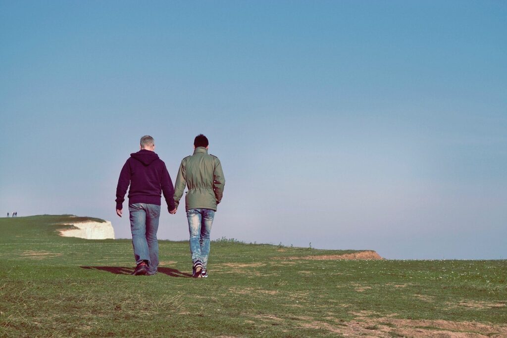 Photograph of a male couple walking along a cliff edge with a blue sky background